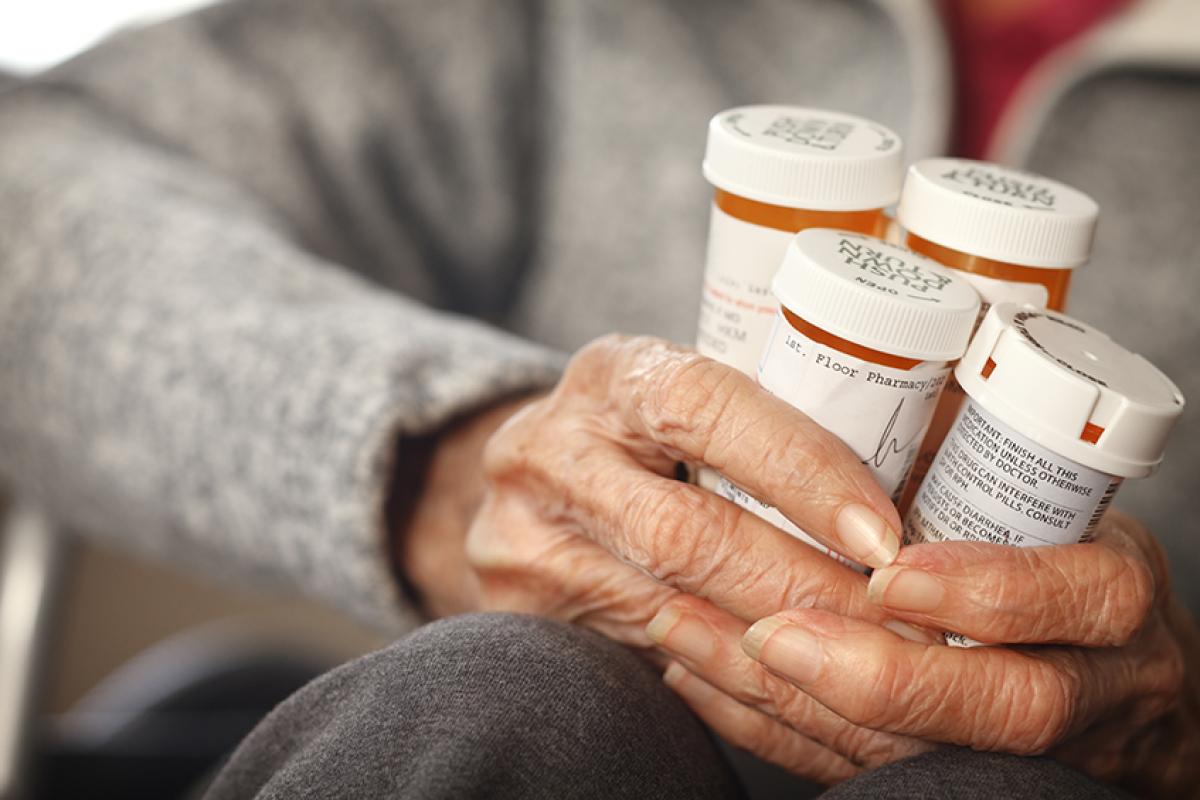 stock photo of an elderly patient's hand holding four bottles of medication