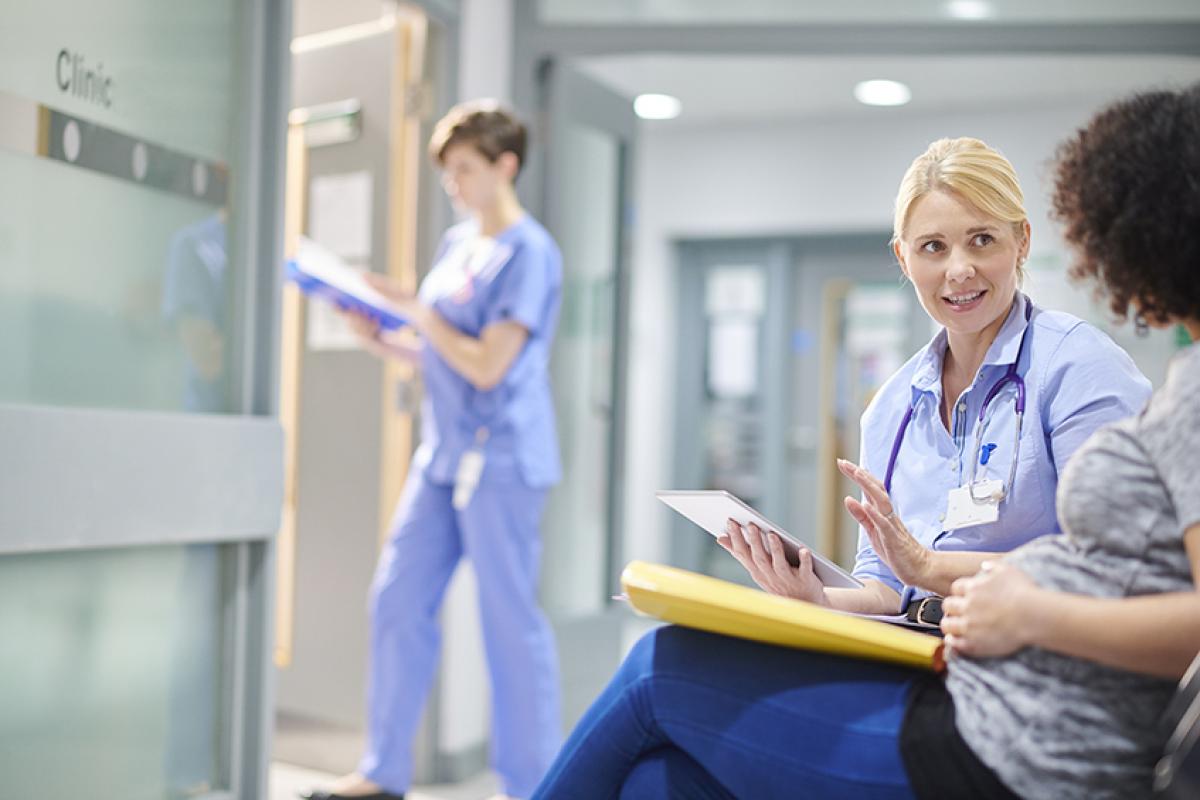 photo showing a nurse talking to a pregnant patient with another female nurse walking into a room